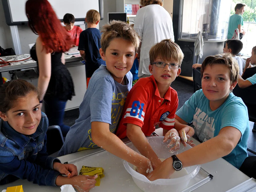 Drei Kinder rühren in einer Schüssel auf dem Tisch.